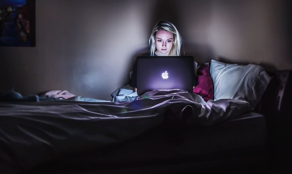woman using laptop in bed to show what not to do to sleeping well with a chronic illness