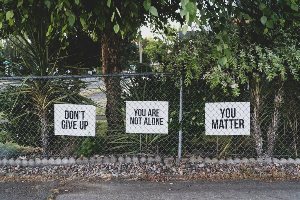 signs on a fence that say, don't give up,  you matter and you are not alone