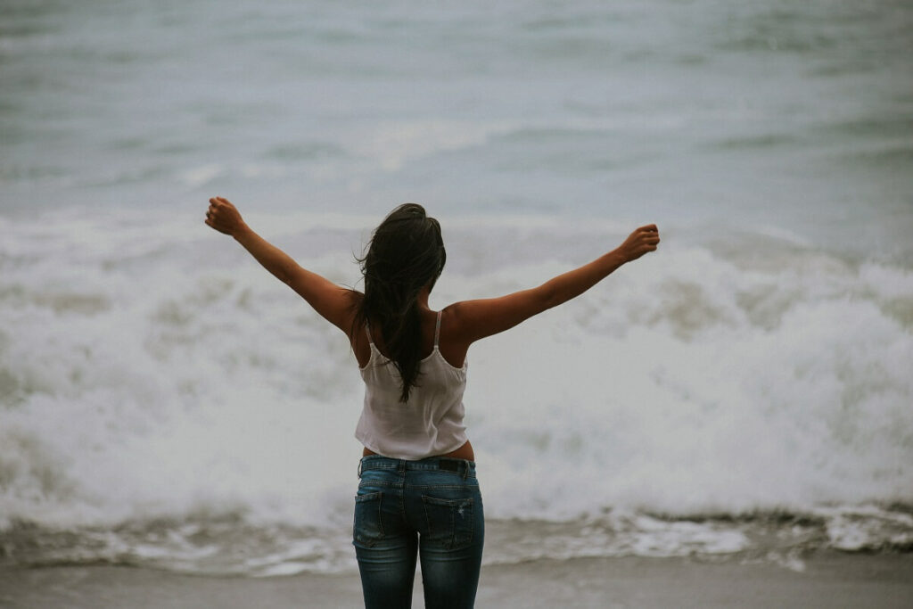 woman with arms open and free in front of ocean to show self-care ideas for autoimmune disease