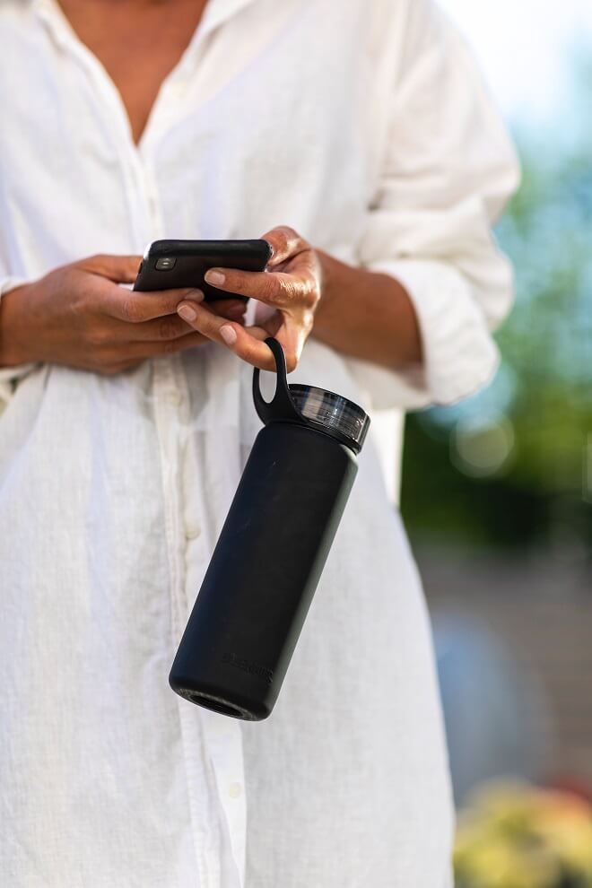 Woman holding her phone and a water bottle for blog post The Lifelong Health Benefits Of Drinking Water
